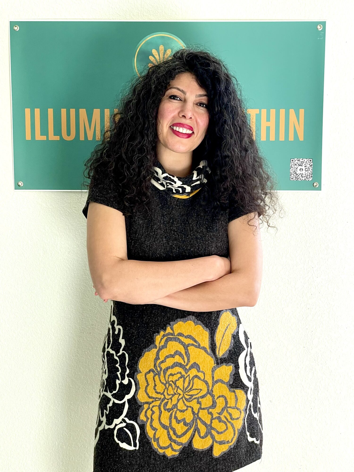 Armineh Turgeon standing with arms crossed in front of the Illumination Within sign