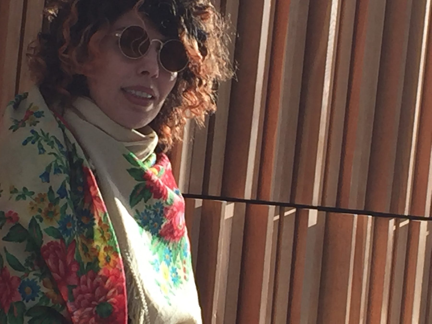 Armineh in a floral shawl against warm wooden slats